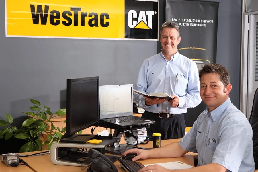 2 male WesTrac employees smiling at desk