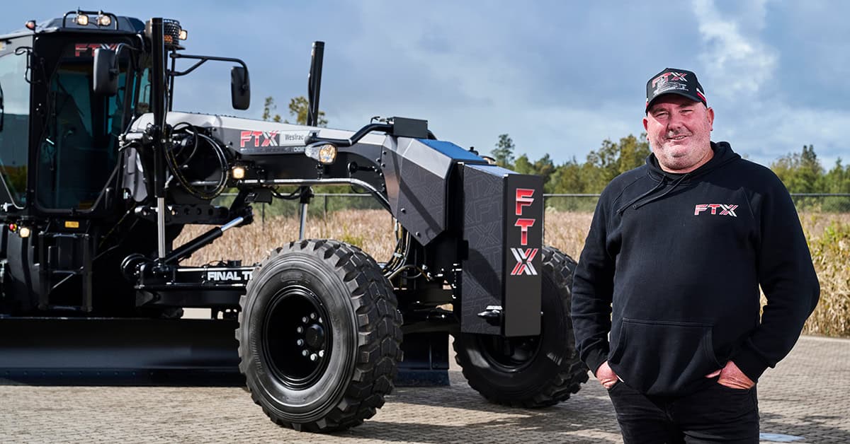 Tom from FTX standing near his black Cat Motor Grader